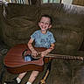 child, smiling, guitar, tattoos, blue_shirt, sneakers, couch, living_room, happy, seated, acoustic_guitar, window, curtains, wood, person, indoors, music, playing, joyful, casual_clothing