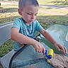 backyard, blue_shirt, boy, casual, chair, child, concentration, daylight, glass_table, grass, house, outdoor, play_dough, playing, sidewalk, summer, table, toy, trees, young