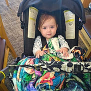 Bella is registered to the contest to win money with this photo: baby, infant, stroller, car_seat, blanket, colorful_blanket, seatbelt, hands, eyes, hair, face, indoor, chair, carpet, floor, buckle, clothing, portrait, calm_expression, hood/canopy