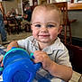 Hudson joined the competition — help win amazing prizes! baby, toddler, child, sippy_cup, blue_cup, smile, blue_eyes, blond_hair, checkered_tablecloth, table, indoor, restaurant, dining, chair, hands, portrait, candid, person, highchair, happy