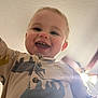 Hudson is registered to the contest to win money with this photo: child, toddler, baby, smiling, face, teeth, onesie, pajamas, dinosaur_pattern, close_up, portrait, indoor, ceiling, ceiling_fan, light_flare, happy, cheerful, hand, button, skin
