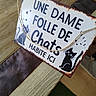 animal, black_cat, cartoon_cat, cat, cozy, cute, decor, floor, french_text, green_rug, home, indoor, peeking, pet, playful, rope, rustic, sign, text, wooden_table
