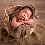 baby, sleeping, basket, brown, fabric, cozy, infant, peaceful, soft, hands, rest, wooden_floor, cute, portrait, newborn, child, wrapped, relaxed, indoors, warm_lighting