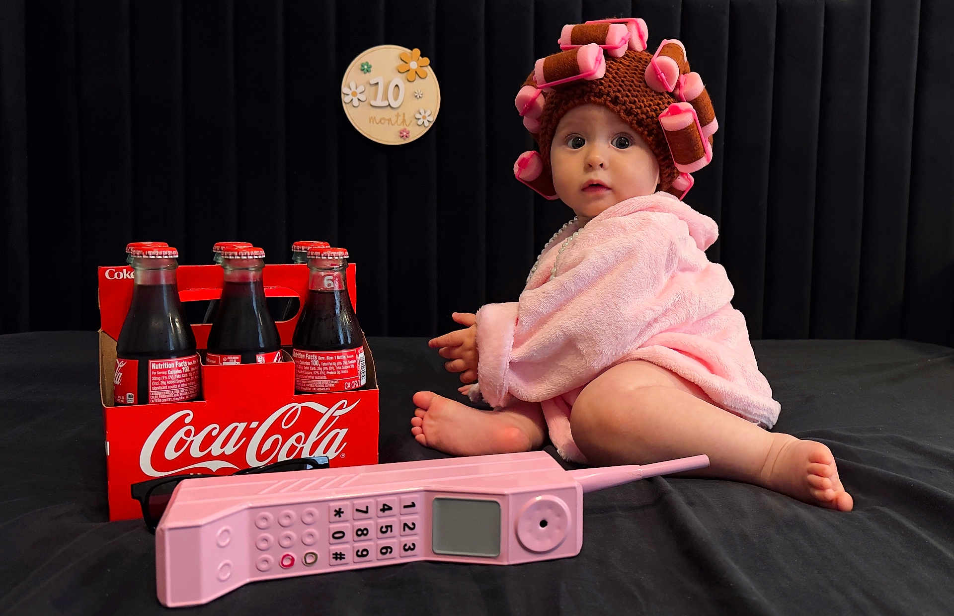 Sofia joined the competition — help win amazing prizes! baby, pink_robe, hair_curlers, vintage_phone, coca_cola, glass_bottles, black_background, sign, 10_month, child, curious, sitting, toy, retro, portrait, indoors, cute, wide_eyes, floor, hat