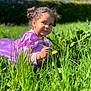 child, toddler, purple_dress, grass, flower, dandelion, outdoor, nature, greenery, sunlight, curly_hair, garden, playful, crouching, daylight, smiling, person, portrait, young_child, happy