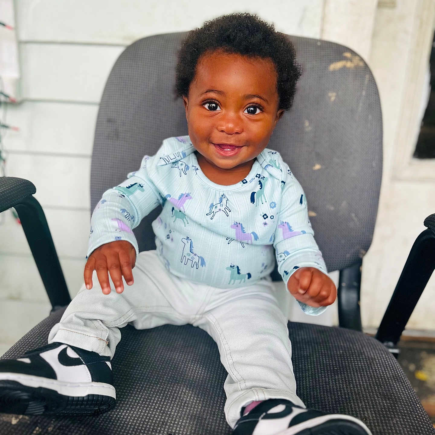 Jahmira is registered to the contest to win money with this photo: black_hair, chair, child, clothing, cute, dark_skin, eyes, feet, hands, happy, indoors, person, portrait, shirt, sitting, smiling, sneakers, toddler, unicorn_pattern, white_pants