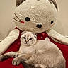 cat, kitten, stuffed_animal, plush_toy, blue_eyes, fur, cute, pet, animal, lying_down, sitting, red_blanket, indoor, portrait, close_up, toy, whiskers, paws, tail, cozy