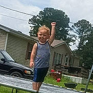Morgan joined the competition — help win amazing prizes! toddler, child, trampoline, backyard, grass, house, car, trees, sky, outdoor, fence, clothing, tank_top, shorts, raised_fist, standing, daytime, play, expression, fun