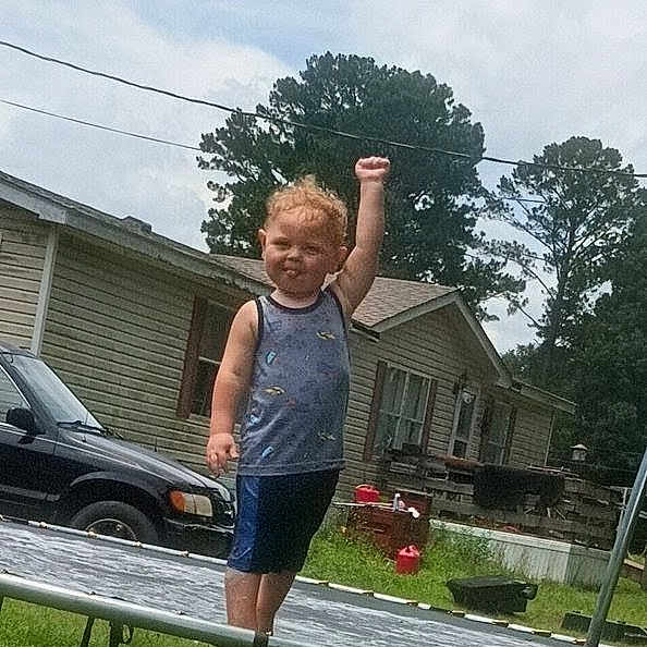 Morgan joined the competition — help win amazing prizes! toddler, child, trampoline, backyard, grass, house, car, trees, sky, outdoor, fence, clothing, tank_top, shorts, raised_fist, standing, daytime, play, expression, fun