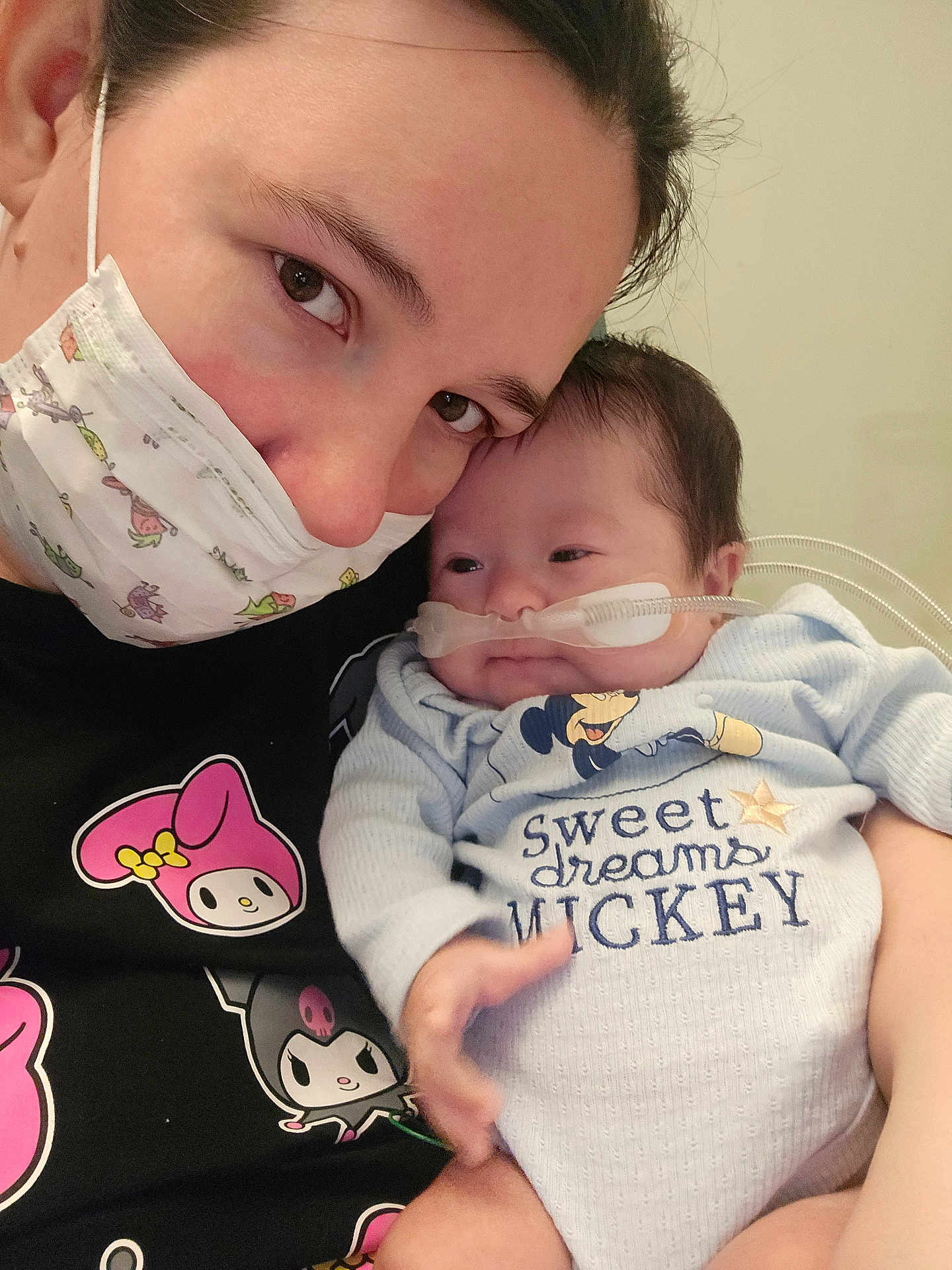 Walker joined the competition — help win amazing prizes! adult, baby, infant, face, mask, nasal_cannula, onesie, mickey, text_on_clothing, holding, cuddling, portrait, close_up, healthcare, hospital_room, hand, eyes, sleepy, parenting, cute