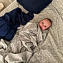 baby, blanket, bed, pillow, smile, face, indoor, pattern, comfort, child, sleeping_area, textile, cute, portrait, rest, cozy, person, fabric, home, relaxation
