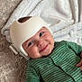 Anya joined the competition — help win amazing prizes! baby, smiling, helmet, green_striped_clothing, infant, lying_down, carpet, blanket, cute, face, child, happy, indoors, soft_texture, hand, headgear, wearing, person, toddler, comfort