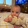 Archie is registered to the contest to win money with this photo: baby, child, plush_toy, bed, blanket, indoors, cute, smiling, chewing, face, hand, person, soft_toy, infant, young_child, cozy, furniture, home, expression, portrait