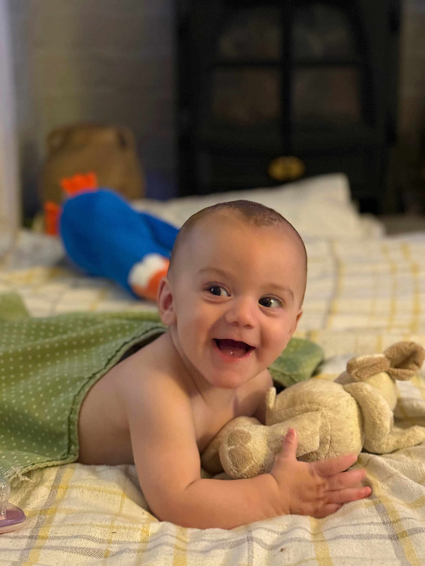 Archie joined the competition — help win amazing prizes! baby, smiling, plush_toy, blanket, bed, indoor, infant, happy, child, soft_toy, person, cute, lying_down, green_blanket, toy, pacifier, face, skin, head, expression
