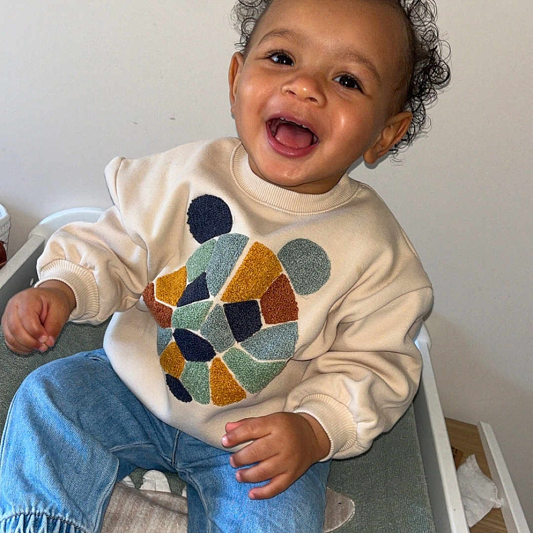 Maël participe au concours pour gagner de l'argent avec cette photo : applique, baby, babylaughing, clothing, coat, face, footwear, happy, head, jeans, laughing, pants, pattern, person, photography, portrait, shoe, sitting, smile, sneaker