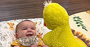 Connor joined the competition — help win amazing prizes! baby, infant, yellow_onesie, smiling, puppet, yellow_duck, cushion, animal_print, nursery, crib, floor, playful, child, happy, indoors, blanket, person, toy, fabric, wooden_furniture