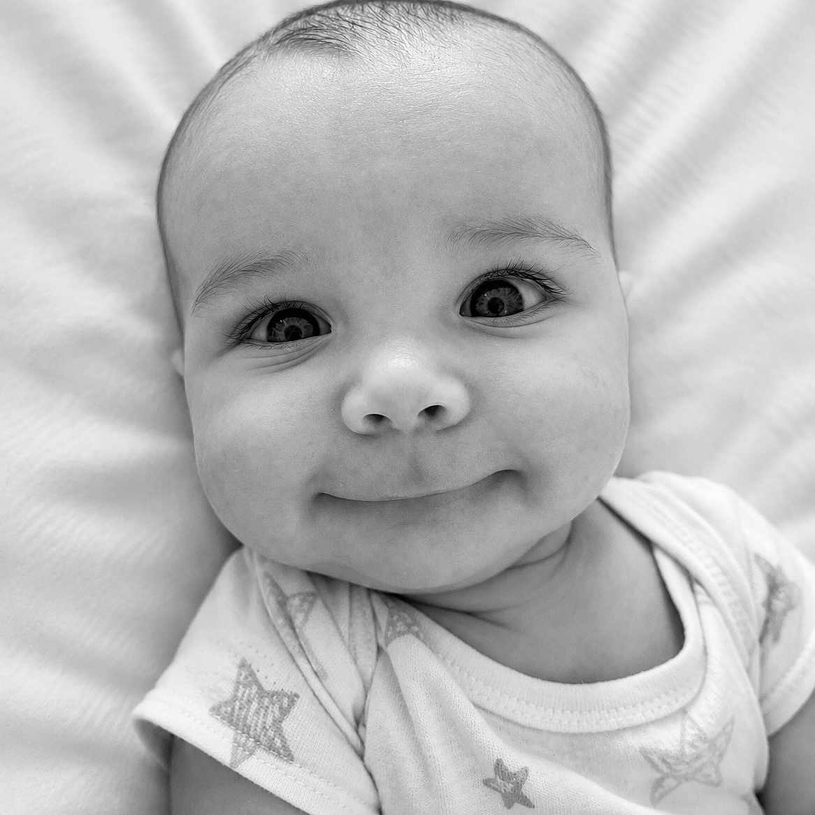 Connor joined the competition — help win amazing prizes! baby, infant, face, portrait, closeup, smile, eyes, onesie, star_pattern, soft, cute, child, newborn, skin, head, expression, lying_down, monochrome, black_and_white, adorable