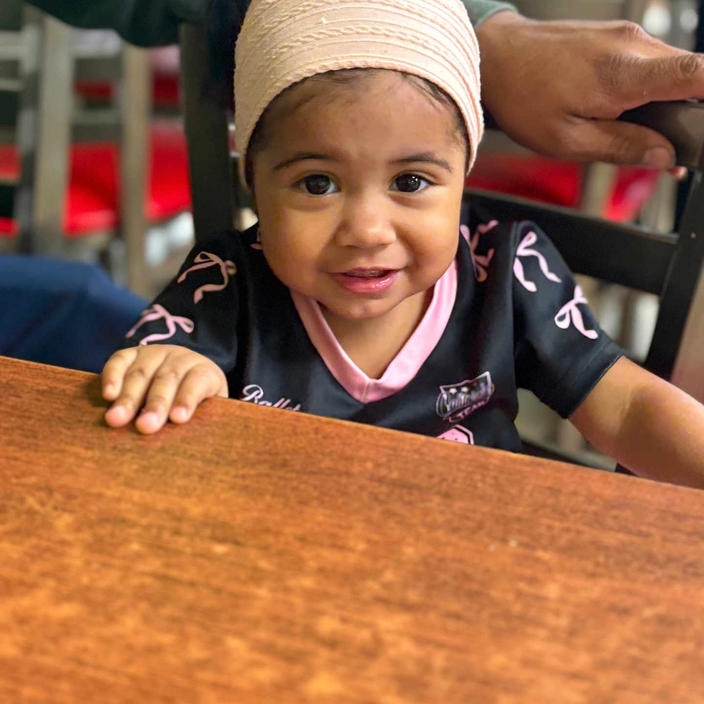 Eva joined the competition — help win amazing prizes! black_shirt, chair, child, clothing, cute, face, furniture, hand, happy, headband, indoor, people, person, pink, portrait, smile, table, toddler, wood, young_child