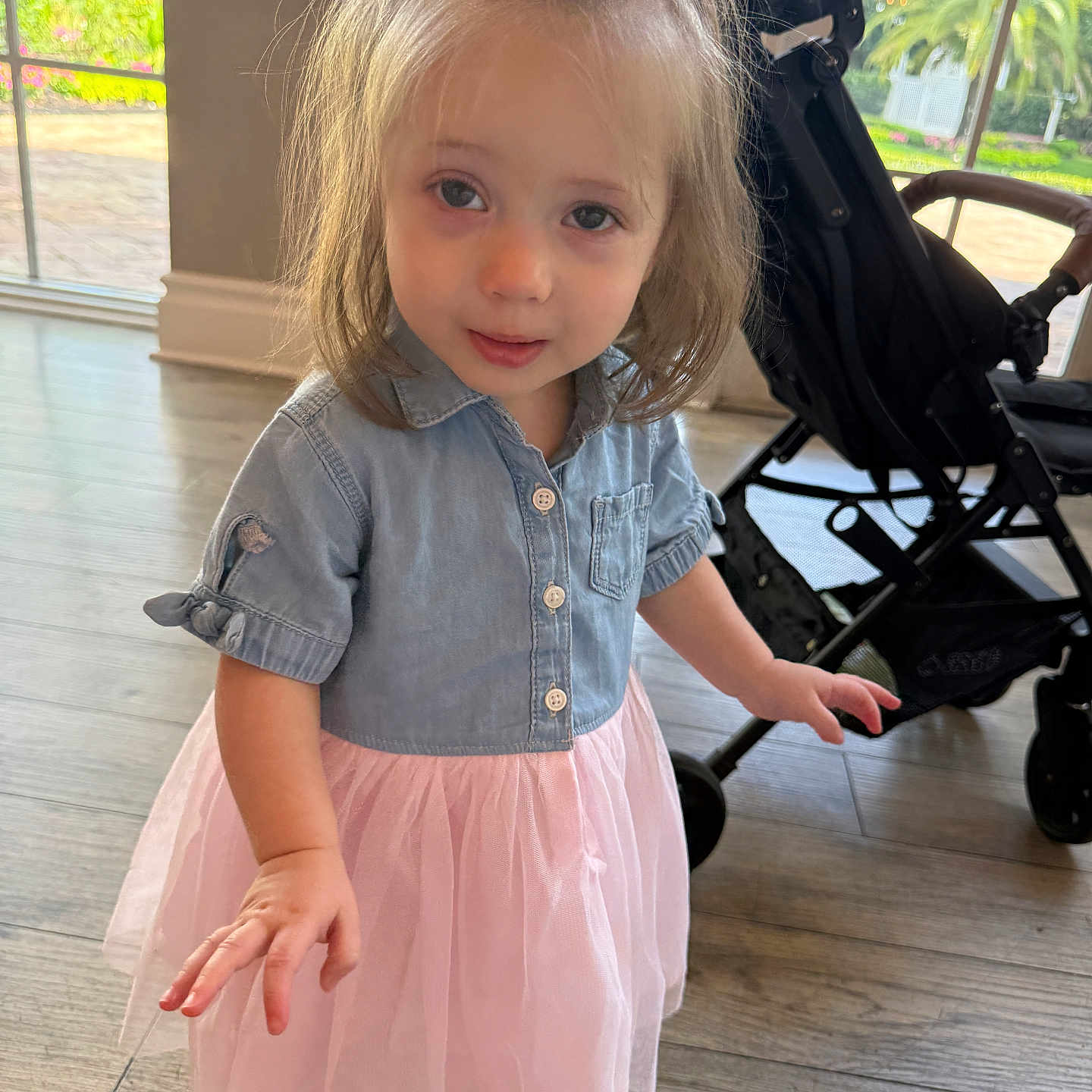 Emma Rose is registered to the contest to win money with this photo: toddler, child, girl, indoor, dress, pink_skirt, denim_shirt, bow, curly_hair, stroller, window, floor, light, innocent, cute, portrait, smiling, person, young, casual