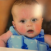 Freddie is registered to the contest to win money with this photo: baby, infant, face, eyes, skin, flotation_device, blue, whale_pattern, water_safety, child, portrait, closeup, curious, expression, young, cute, head, human, indoors, person