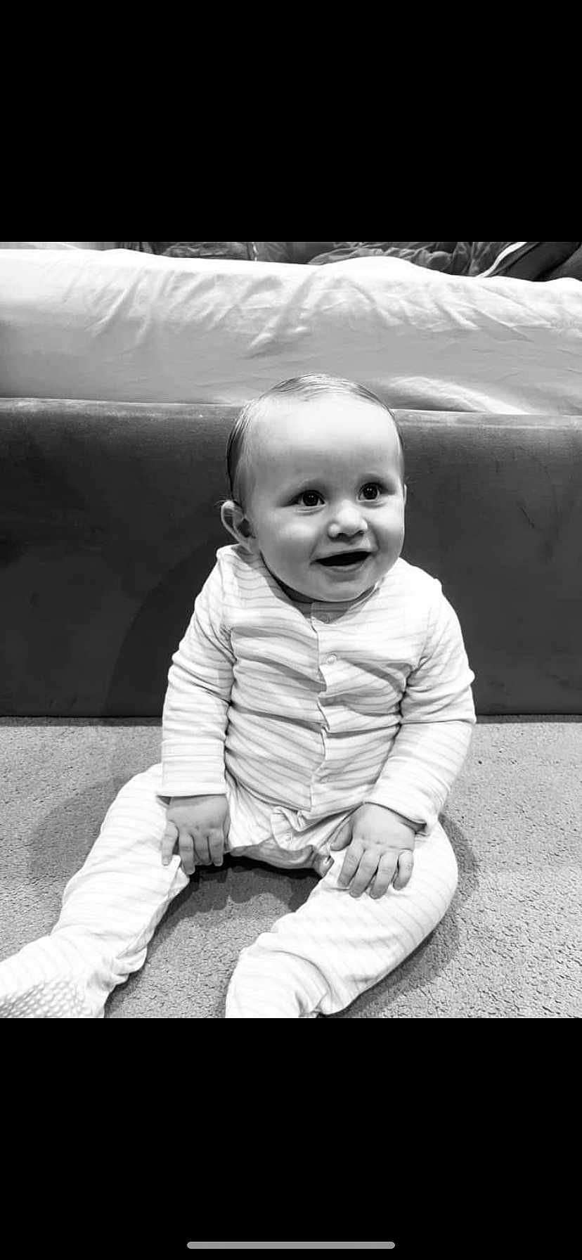 Teddy joined the competition — help win amazing prizes! baby, child, smiling, pajamas, striped_clothing, carpet, sitting, indoor, face, happy, infant, cute, young_child, person, furniture, couch, monochrome, black_and_white, portrait, home