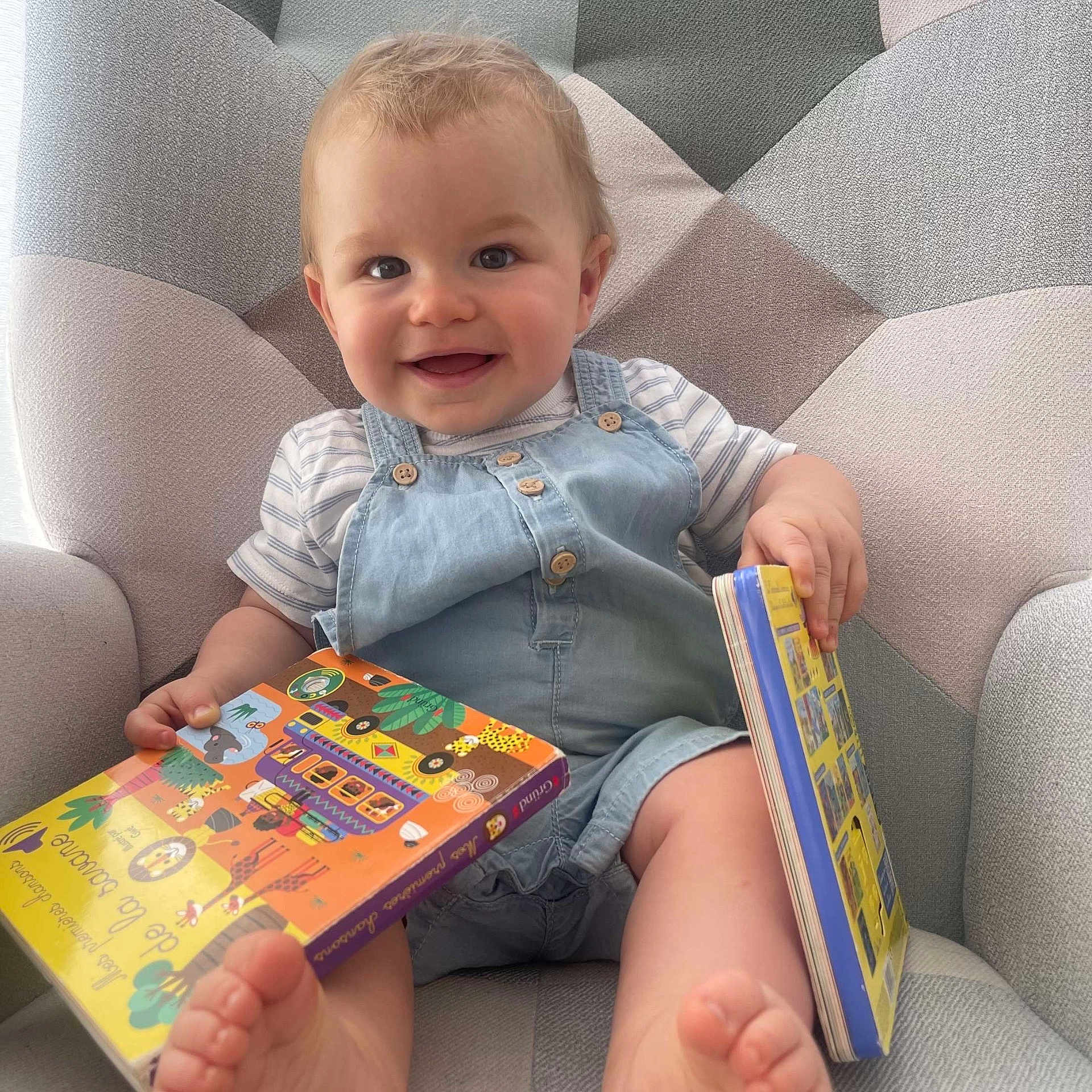 Leo a rejoint le concours — aidez-le/la à gagner de superbes lots ! baby, child, smile, book, reading, armchair, foot, clothing, denim_overall, striped_shirt, indoor, happy, cute, infant, person, face, hand, toes, furniture, playful