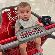 Layne joined the competition — help win amazing prizes! baby, shopping_cart, child, store, aisle, floor, wallet, hand, foot, clothing, safety_bar, red, gray, curious, indoor, person, seat, plastic, shopping, retail