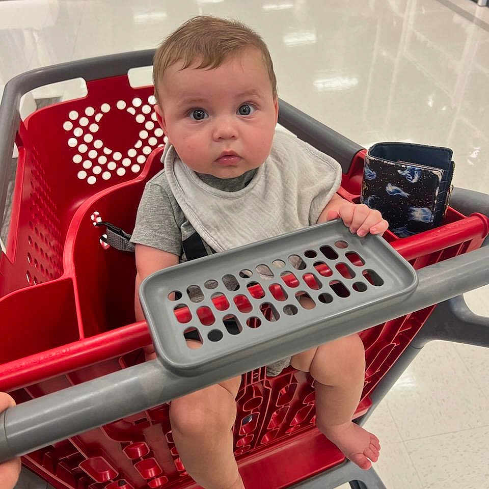 Layne joined the competition — help win amazing prizes! aisle, baby, child, clothing, curious, floor, foot, gray, hand, indoor, person, plastic, red, retail, safety_bar, seat, shopping, shopping_cart, store, wallet