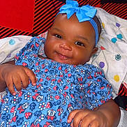 Sariyah is registered to the contest to win money with this photo: baby, child, smiling, blue_dress, headband, bow, bed, blanket, pillow, pattern, floral, happy, infant, cute, clothing, person, indoors, skin, hand, lying_down
