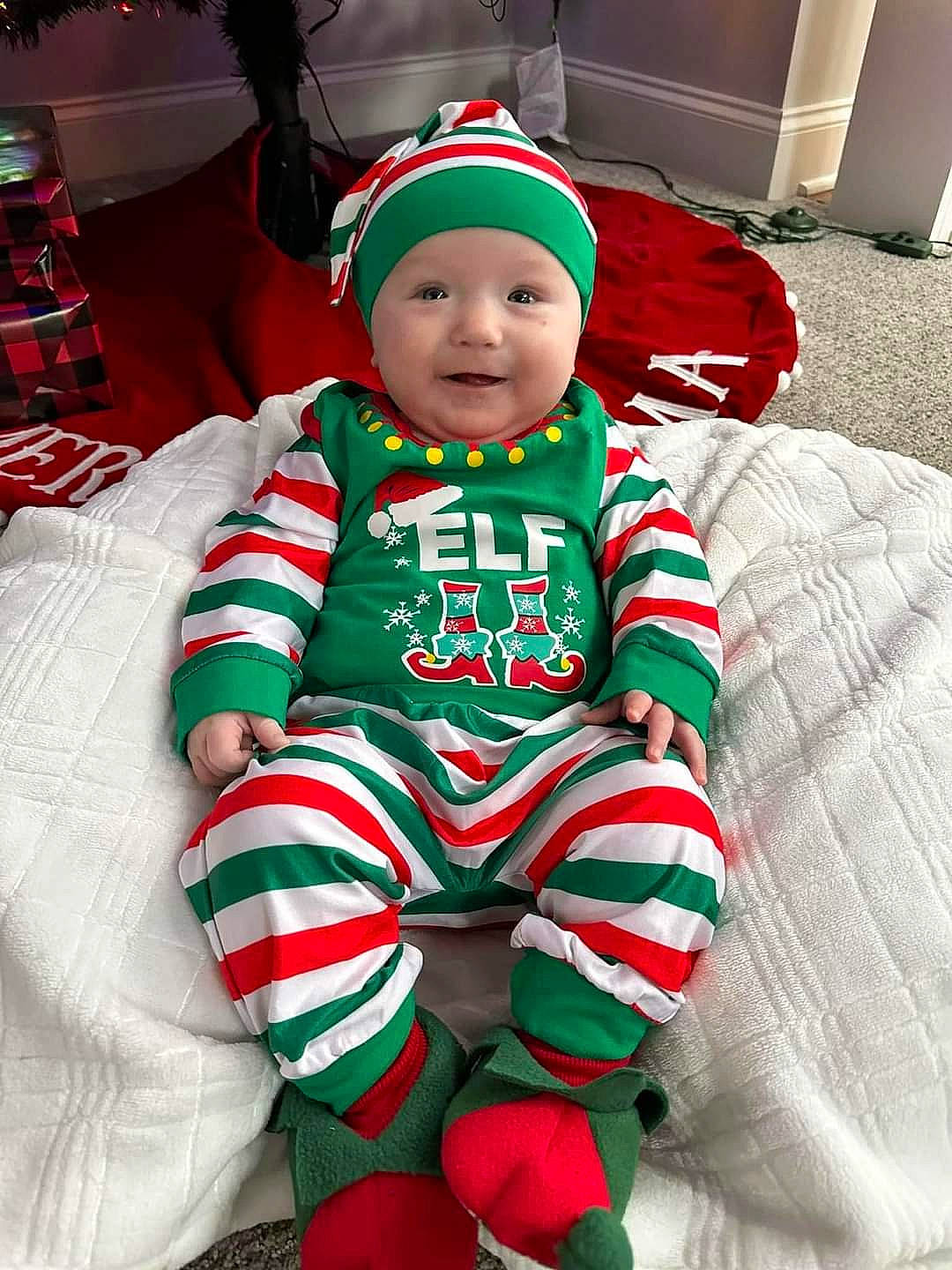 Brooks is registered to the contest to win money with this photo: baby, baby_toddler_clothing, christmas, christmas_decoration, christmas_elf, christmas_eve, costume_hat, event, face, facial_expression, green, happy, headwear, holiday, lap, pattern, person, red, sleeve, smile