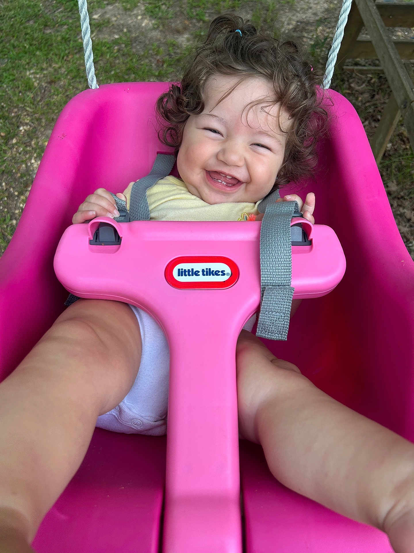 Mia is registered to the contest to win money with this photo: baby, child, toddler, swing, pink, outdoor, grass, curly_hair, smiling, happy, play, seat, toy, strap, person, face, legs, hands, daylight, nature