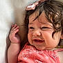 baby, child, smile, curly_hair, bow, pink_bow, coral_dress, floral_pattern, hand, face, cheek, cushion, close_up, happy, infant, skin, portrait, resting, indoors, cute