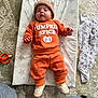 baby, infant, orange_clothing, pumpkin_spice, hat, brown_hat, star_pattern, mat, carpet, toy, orange_toy, white_shoes, denim, knees, patterned_cloth, floor, indoors, cute, lying_down, child