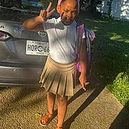 Bailee is registered to the contest to win money with this photo: backpack, car, child, driveway, girl, grass, headband, house, license_plate, outdoor, peace_sign, person, pleated_skirt, portrait, sandals, school_uniform, shadow, sidewalk, sunlight, white_polo