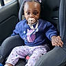 Hailee is registered to the contest to win money with this photo: toddler, child, car_seat, pacifier, purple_bows, sweatshirt, fox_design, pants, socks, shoes, hand, seatbelt, vehicle_interior, window, curious, indoor, cute, baby, person, portrait