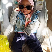 Hailee is registered to the contest to win money with this photo: baby, baby_seat, child, clothing, cool_pose, cute, denim_jacket, fashion, headband, indoor, light_and_shadow, monkey_design, pink, portrait, relaxing, sunglasses, sweater, toddler, wooden_floor, yellow_plastic_bag
