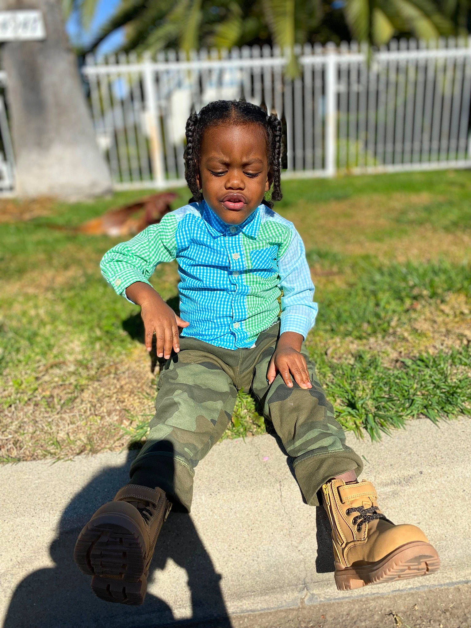 Logan is registered to the contest to win money with this photo: baby_toddler_clothing, boot, child, denim, fence, footwear, fun, grass, happy, human_leg, leisure, people_in_nature, person, shoe, sitting, sleeve, sneakers, t_shirt, thigh, toddler