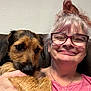 Max is registered to the contest to win money with this photo: woman, dog, glasses, pink_shirt, smile, pet, indoor, close_up, face, hand, fur, friendly, happy, casual, portrait, human, animal, companionship, couch, background