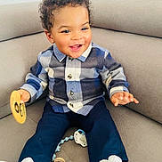 Mateus participe au concours pour gagner de l'argent avec cette photo : baby, beige_couch, casual_clothing, child, comfortable, curly_hair, cute, happy, indoor, navy_pants, pacifier, plaid_shirt, playful, portrait, sitting, smiling, toddler, white_shoes, wooden_toy, young_child