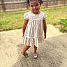child, girl, smiling, outdoor, dress, pigtails, grass, fence, concrete, footwear, happy, portrait, young_child, person, sunlight, playful, nature, cute, summer, standing