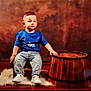 toddler, child, blue_tshirt, jeans, white_sneakers, wooden_barrel, chair, fluffy_rug, studio, portrait, indoor, serious_expression, brown_background, floor, young_child, casual_clothing, sitting, hand_on_barrel, cute, small_chair