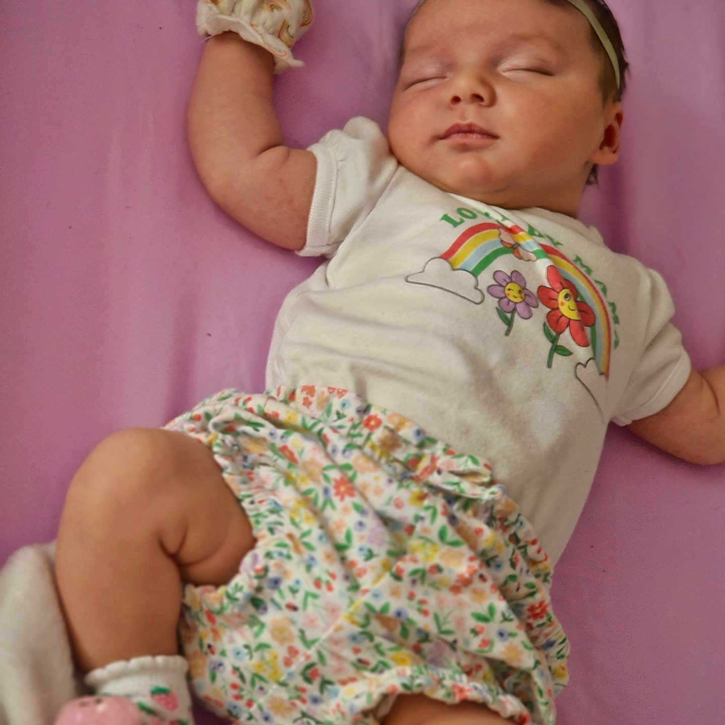 Zhalani is registered to the contest to win money with this photo: adorable, baby, child, clothing, cute, floral_skirt, flowers, headband, infant, lying_down, mitten, newborn, peaceful, purple_background, rainbow, resting, sleeping, sock, soft, white_shirt