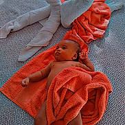 Layhann a rejoint le concours — aidez-le/la à gagner de superbes lots ! baby, towel, heart_shape, bed, blanket, infant, patterned_bedspread, orange_towel, skin, foot, hand, relaxing, lying_down, cozy, soft_texture, indoor, cute, resting, newborn, comfortable
