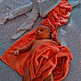baby, towel, heart_shape, bed, blanket, infant, patterned_bedspread, orange_towel, skin, foot, hand, relaxing, lying_down, cozy, soft_texture, indoor, cute, resting, newborn, comfortable