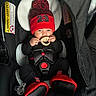 Jakari is registered to the contest to win money with this photo: baby, infant, car_seat, knit_hat, pacifier, red_booties, black_clothing, child, cute, indoors, sitting, safety_harness, headwear, warm_clothing, small_hands, closeup, portrait, cozy, child_protection, adorable