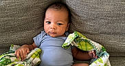 Jakari is registered to the contest to win money with this photo: baby, blanket, blue_clothing, child, comfort, couch, cozy, cute, fabric, home, indoor, infant, looking_at_camera, person, portrait, relaxing, sitting, small_hands, texture, young