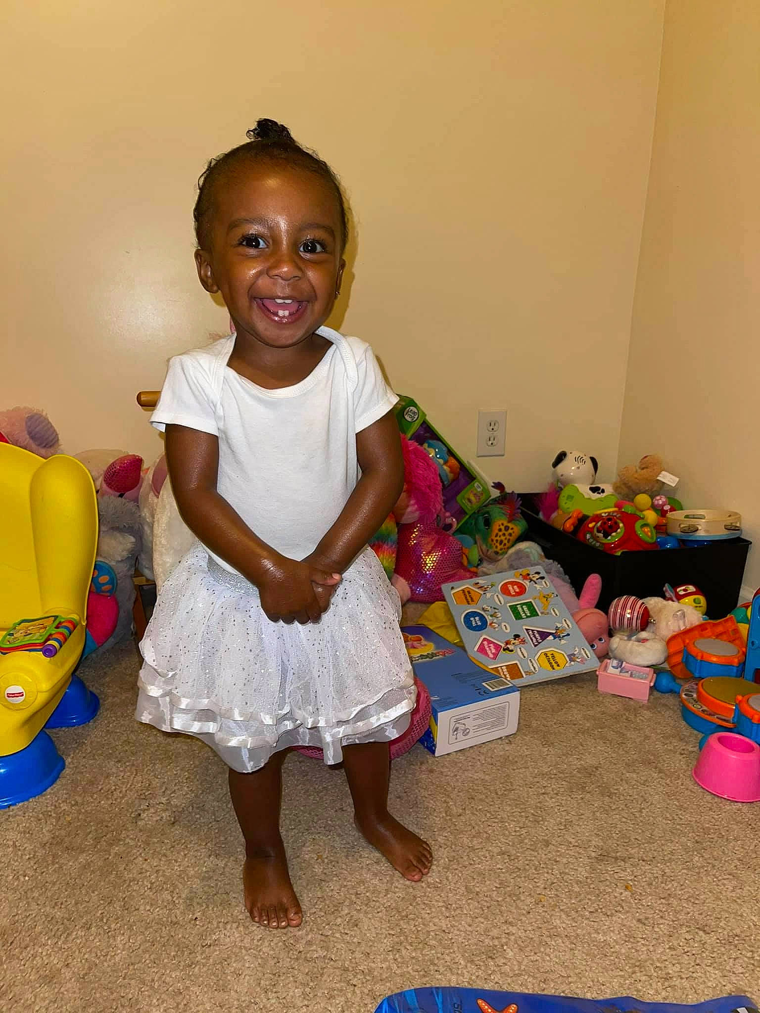 Lani is registered to the contest to win money with this photo: baby_toddler_clothing, child, dress, event, face, flooring, fun, happy, head, human_body, joy, pattern, person, pink, room, sandal, sitting, smile, stuffed_toy, toddler