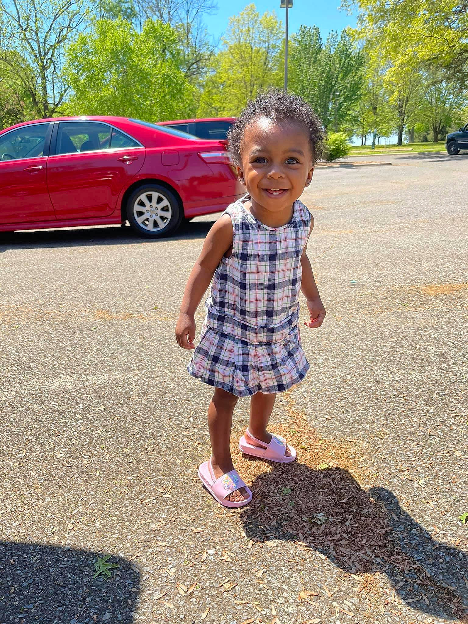 Lani is registered to the contest to win money with this photo: asphalt, car, fun, grass, infrastructure, joy, land_vehicle, line, motor_vehicle, person, public_space, road, road_surface, sky, summer, tints_and_shades, tire, toddler, tree, vehicle