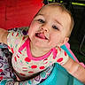 baby, child, tongue_out, onesie, baby_walker, playful, rosy_cheeks, indoor, colorful, patterned_clothing, infant, cute, smiling, face, person, seat, toy, closeup, happy, young_child