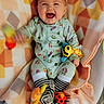 baby, smiling, pajamas, toy, blanket, colorful, infant, happy, lying_down, plush_toy, patterned_clothing, striped_socks, cute, child, indoors, cheerful, face, playful, small_toys, soft_texture